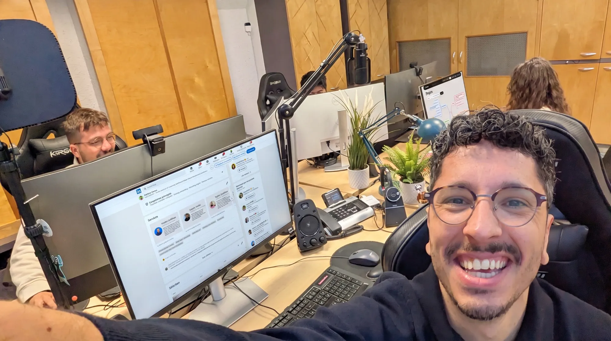 Anthony au bureau, en selfie, des collègues au travail derrière lui